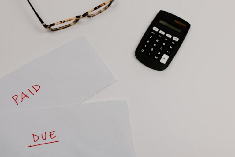 Top view of household financial papers labeled Paid and Due beside a calculator and reading glasses